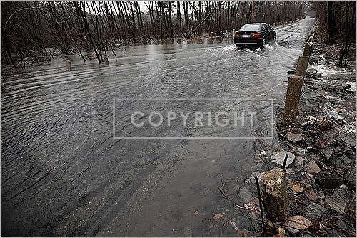 A car drove by the overflowing Crosby Pond on Cambridge Turnpike.