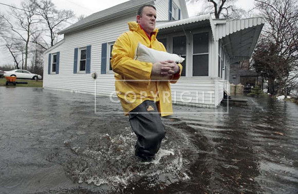 Rob Arneson carries a sandbag as he walks through a flooded area along Staples Shore Road in Lakeville, Mass., where 10 residents had been evacuated.